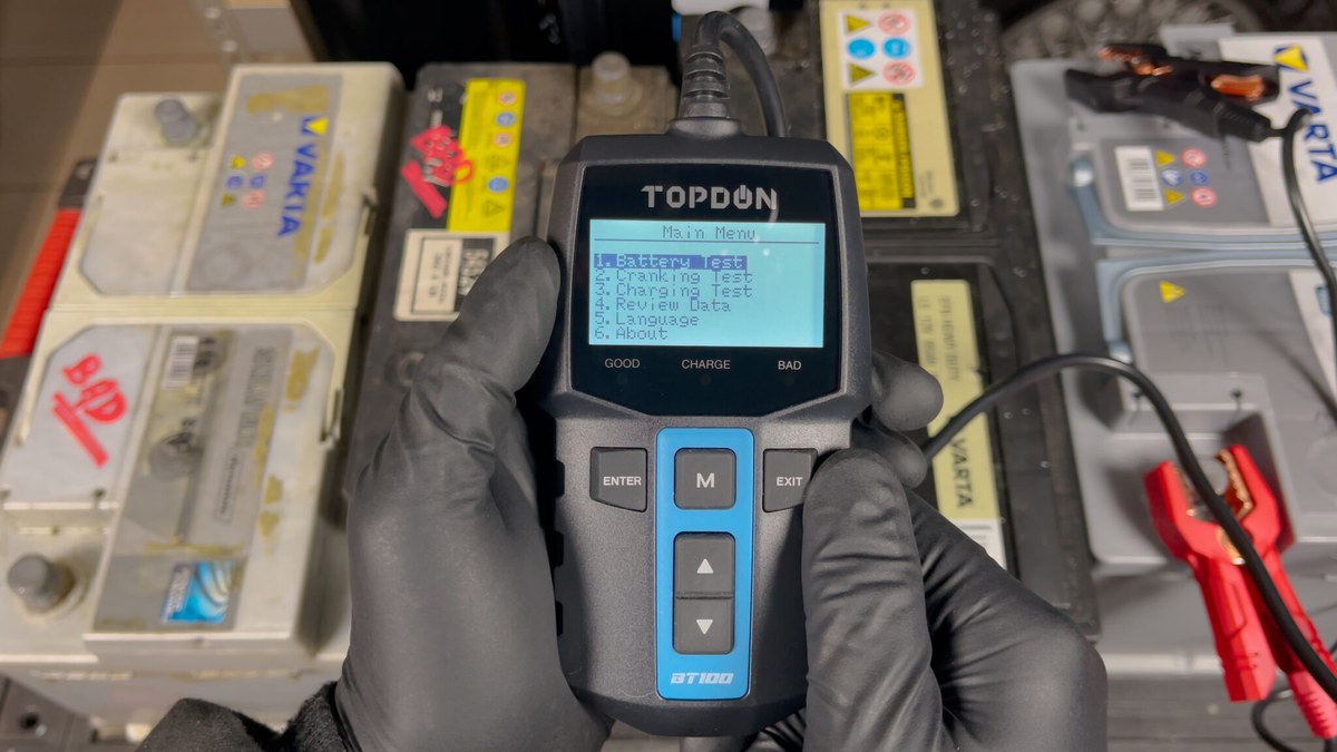 Technician using a TOPDON scanner to test a car battery during a step-by-step diagnostic check