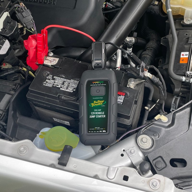 Portable jump starter connected to a car battery during OBD2 diagnostics with a smartphone app nearby