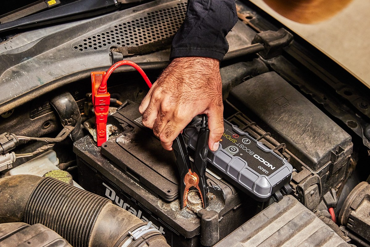Portable jump starter with warning light beside a car battery showing corrosion and swollen casing