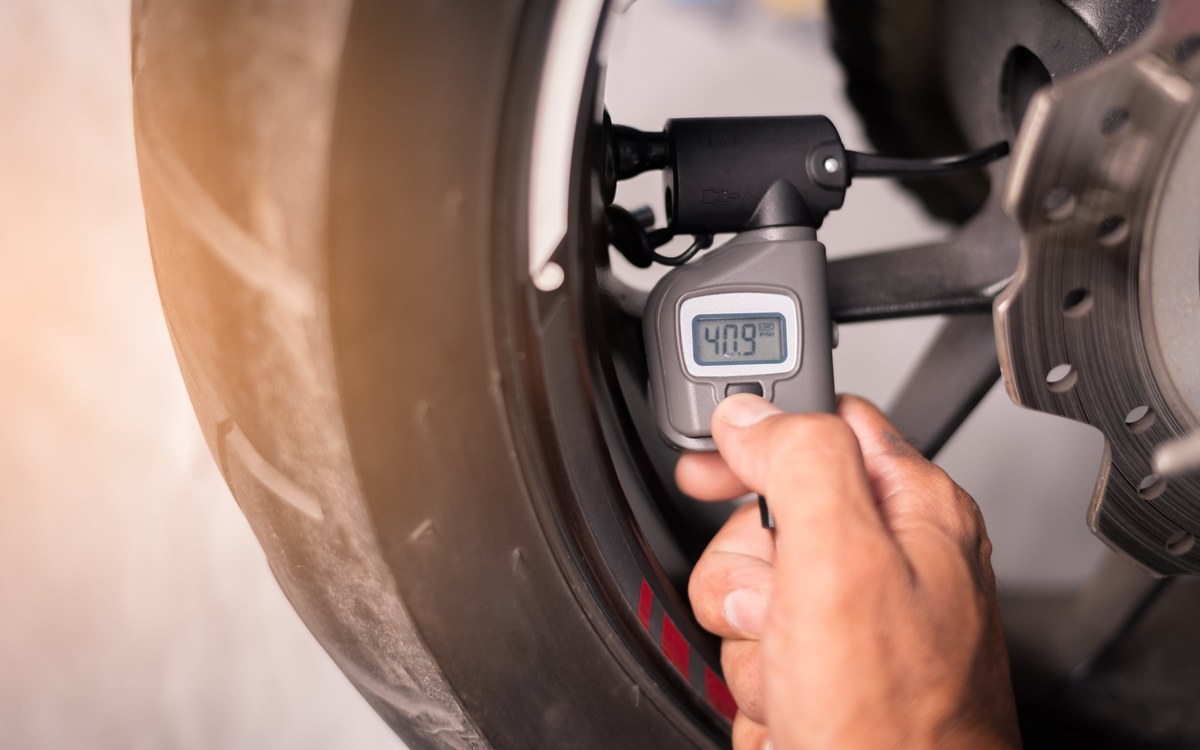 Driver checking tire pressure with a gauge next to a tire pressure warning light