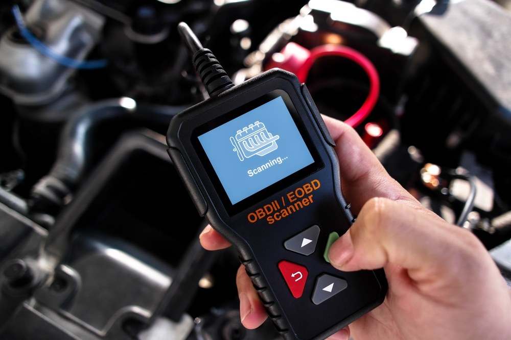 Mechanic checking battery, power, and safety before using an OBD2 scanner on a car