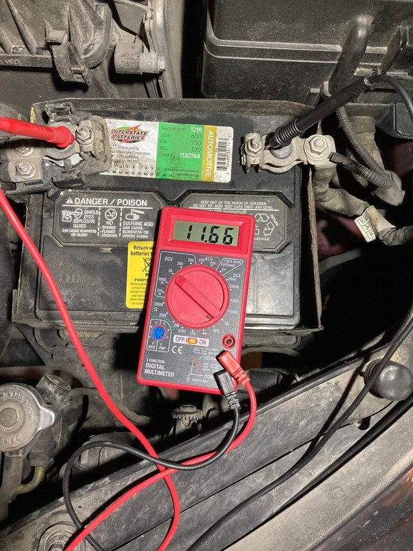 Mechanic checking car battery voltage and terminal connections under an open hood