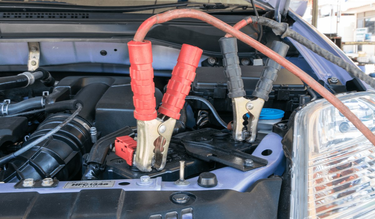 Driver checking jump starter clamps and car battery terminals for correct polarity before reconnecting