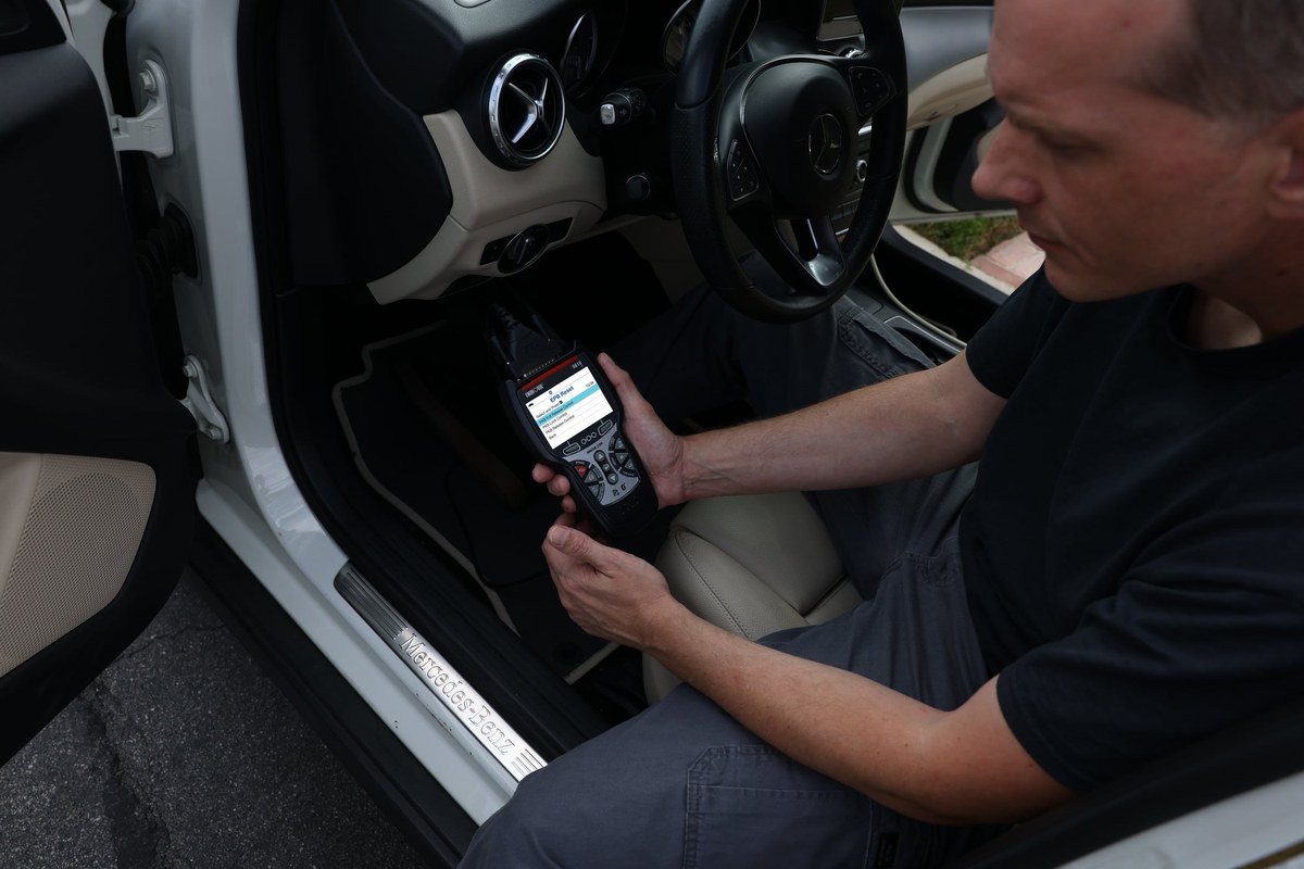 OBD2 scanner plugged into car's diagnostic port, displaying oil life reset option