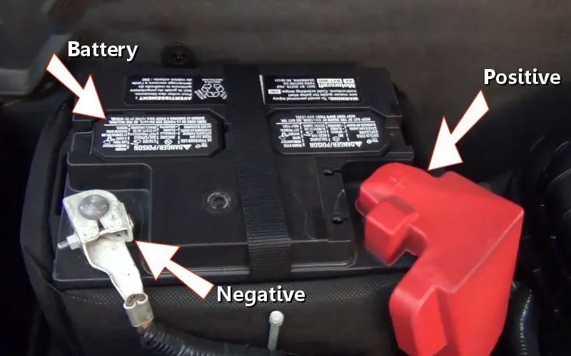 Technician connecting multimeter leads to a car battery terminal while wearing safety gloves