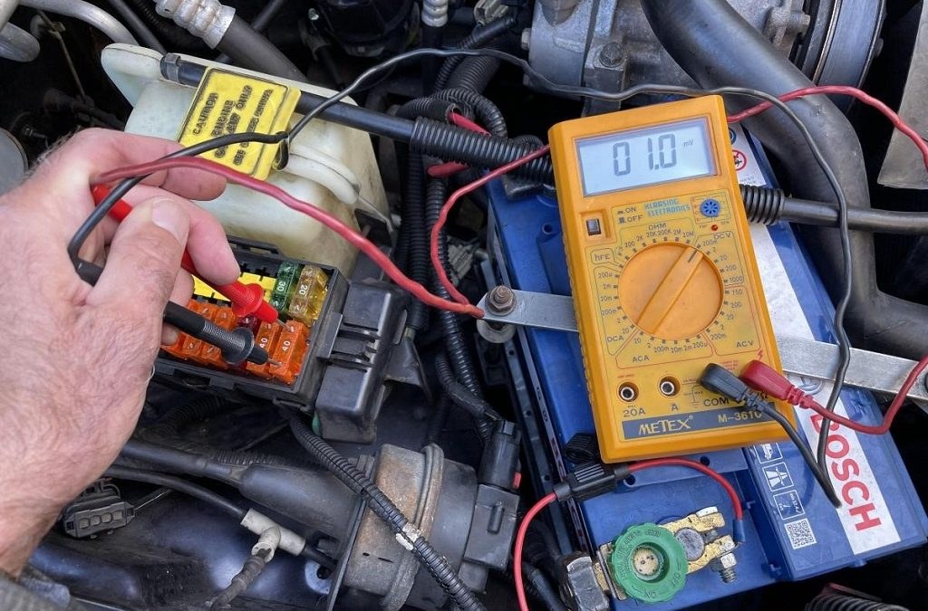 Multimeter testing car battery for parasitic draw with interior lights and control modules as common culprits