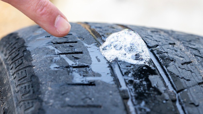 Close-up of a car tire with a nail embedded in the tread, indicating a slow puncture.